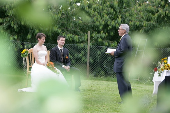 hochzeitspaar sitzt zu zwei auf einer bank vor ihnen steht der Pfarrer mit einer bibel in der hand