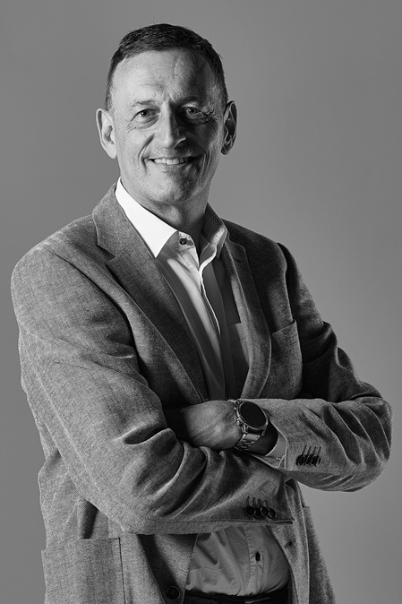 schwarz-weiss portrait eines geschäftsmannes mit weissem hemd und grauem jacket, lächelnd mit verschränkten armen